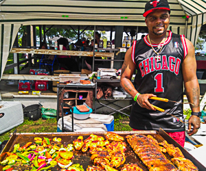 Man cooking chicken, ribs, and vegetables over large grill