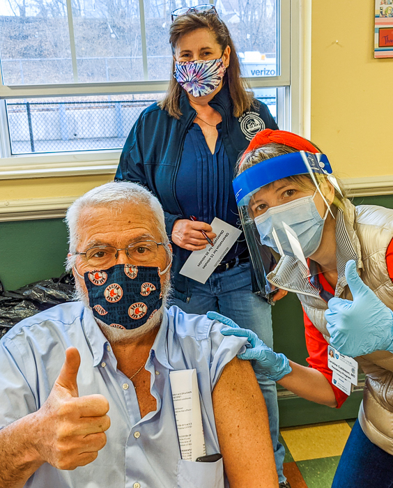 Glen Jalbert, Fairweather resident, and Caroline Cubbison, resident physician at North Shore Medical, give a thumbs up after Glen is vaccinated. Sharon Cameron, Director of the Peabody Health Department, looks on.